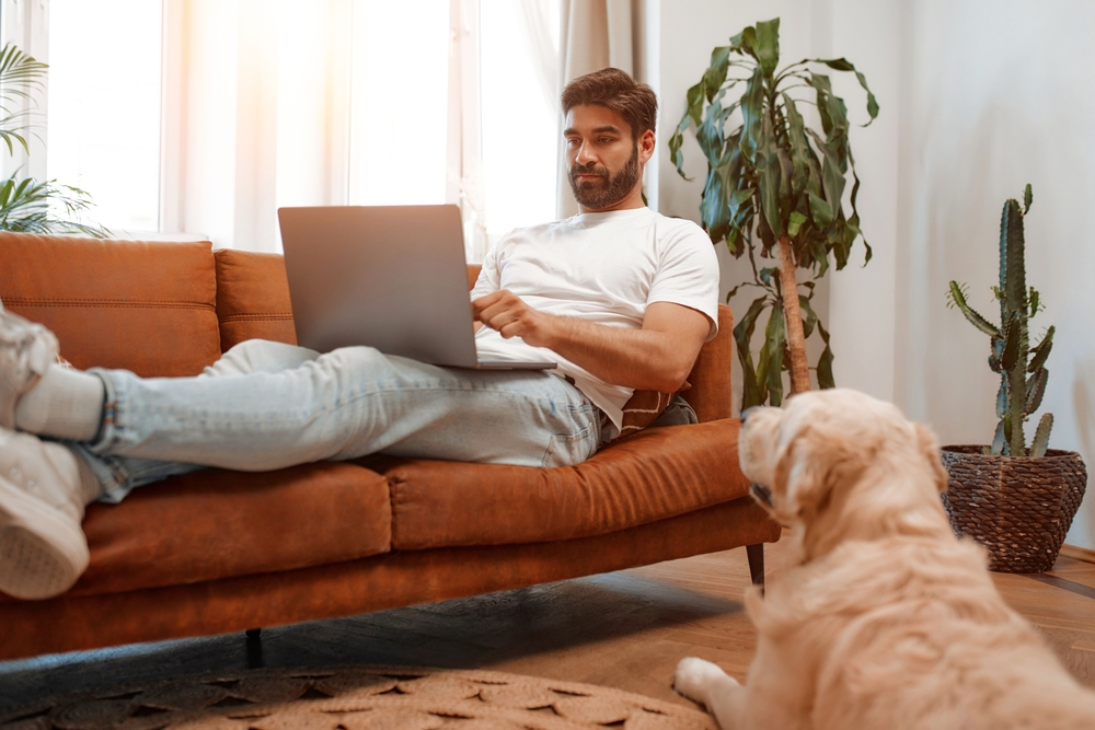 Man working on laptop at home with Labrador dog resting nearby